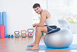 Smiling man sitting on exercise ball and looking at camera