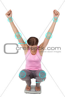 Composite image of full length of a young woman cheering on weight scale