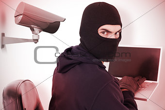 Composite image of hacker sitting and hacking laptop