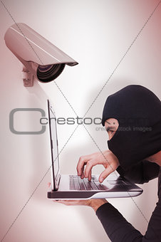 Composite image of focused burglar with balaclava typing on laptop