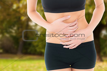 Composite image of mid section of a fit young woman with stomach pain