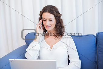 Pretty brunette speaking on the phone while using her laptop