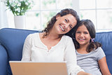 Happy mother and daughter sitting on the couch and using laptop