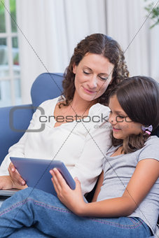 Happy mother and daughter sitting on the couch and using tablet