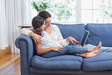 Happy mother and daughter sitting on the couch and using laptop