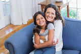 Happy mother and daughter sitting on the couch and smiling at camera