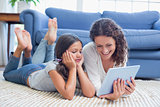 Happy mother and daughter lying on the floor and using tablet