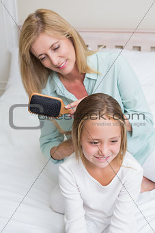 Smiling mother brushing her daughters hair