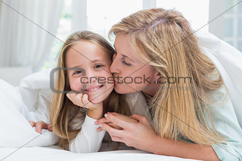 Mother kissing her daughter on the cheek in the bed