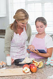 Happy mother and daughter preparing cake together with tablet