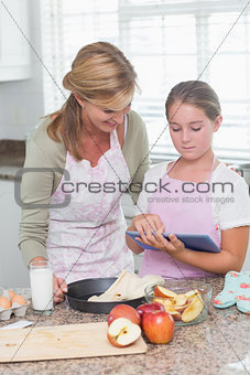 Happy mother and daughter preparing cake together with tablet