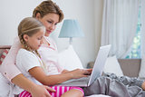 Mother and daughter using laptop in bed