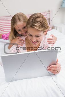 Mother and daughter using tablet together on bed