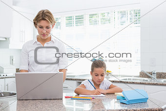 Little girl doing her homework with mother using laptop