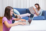 Mother reading news with daughter using laptop