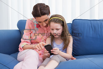 Mother and daughter using smartphone on couch