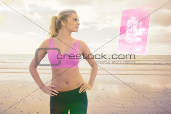 Composite image of toned woman with hands on hips on beach