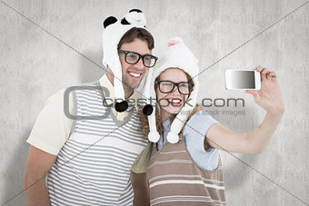 Composite image of geeky hipster couple taking selfie with smartphone