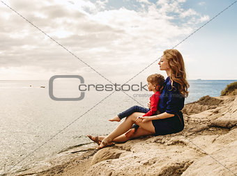 Mother and daughter sitting on a rock near the sea