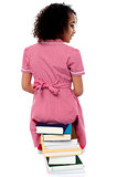 Back pose of a girl sitting on a pile of books