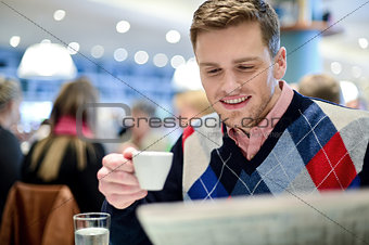 Smiling man reading newspaper at restaurant
