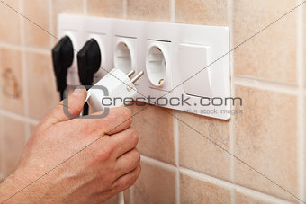 Hand plugging power cord into wall outlet
