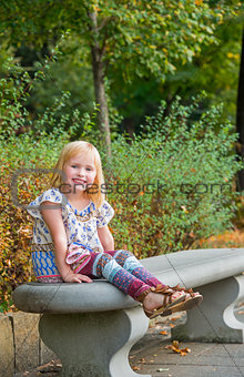 Portrait of smiling girl sitting on bench in city park