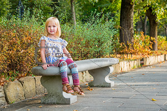 Portrait of girl sitting on bench in city park
