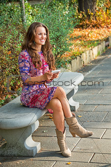 Happy young woman writing sms while sitting in city park