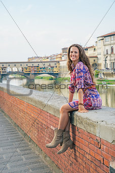Happy young woman sitting near ponte vecchio in florence, italy