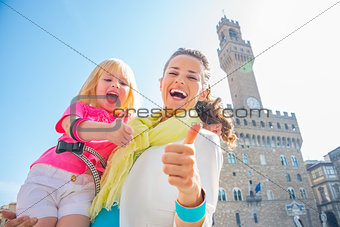 Happy mother and baby girl showing thumbs up in front of palazzo