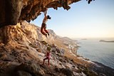 Young woman lead climbing on overhanging cliff, female partner belaying