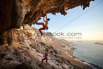 Young woman climbing on cliff, female partner belaying