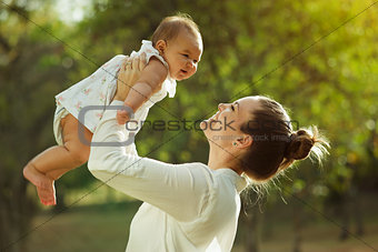 Mother Lifting Up And Turning Around Little Baby Daughter In Par