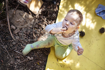 Little boy biting a cone while sitting on a touristic mat on the ground