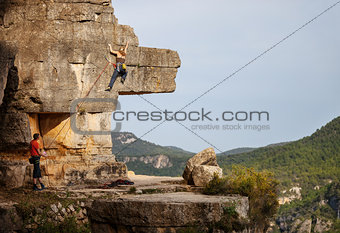 Young woman climbing on cliff, male partner belaying