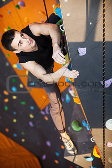 Young man practicing rock-climbing in climbing gym indoors