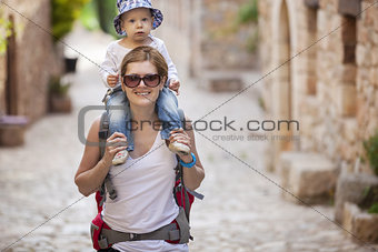 Young Caucasian woman tourist carrying her little son on shoulders