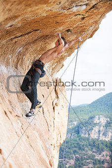 Young man clipping rope while clinging to cliff under ledge, challenging part of route