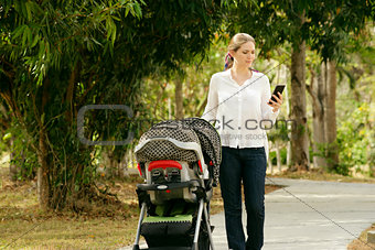 Mother With Baby In Pushchair Typing Message On Phone