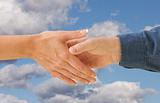 Man and woman shaking hands on cloud filled blue sky background.
