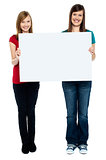 Pair of good looking women holding whiteboard