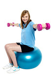 Girl sitting on pilates ball and doing dumbbells