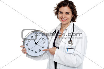 Pretty doctor pointing out time on wall clock