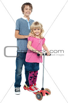 Brother holding her sister as she rides her toy scooter