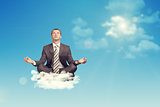 Businessman sitting in lotus position on cloud, looking up