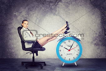Businesswoman sits in chair. Put your feet up on big red alarm clock