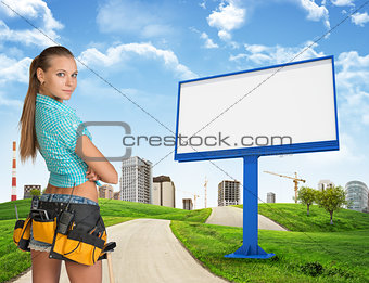 Girl builder in toolbelt. Large billboard, road, grass hills and city