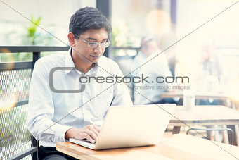 Man using laptop computer at outdoor cafe.