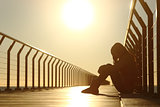 Sad teenager girl depressed sitting in a bridge at sunset